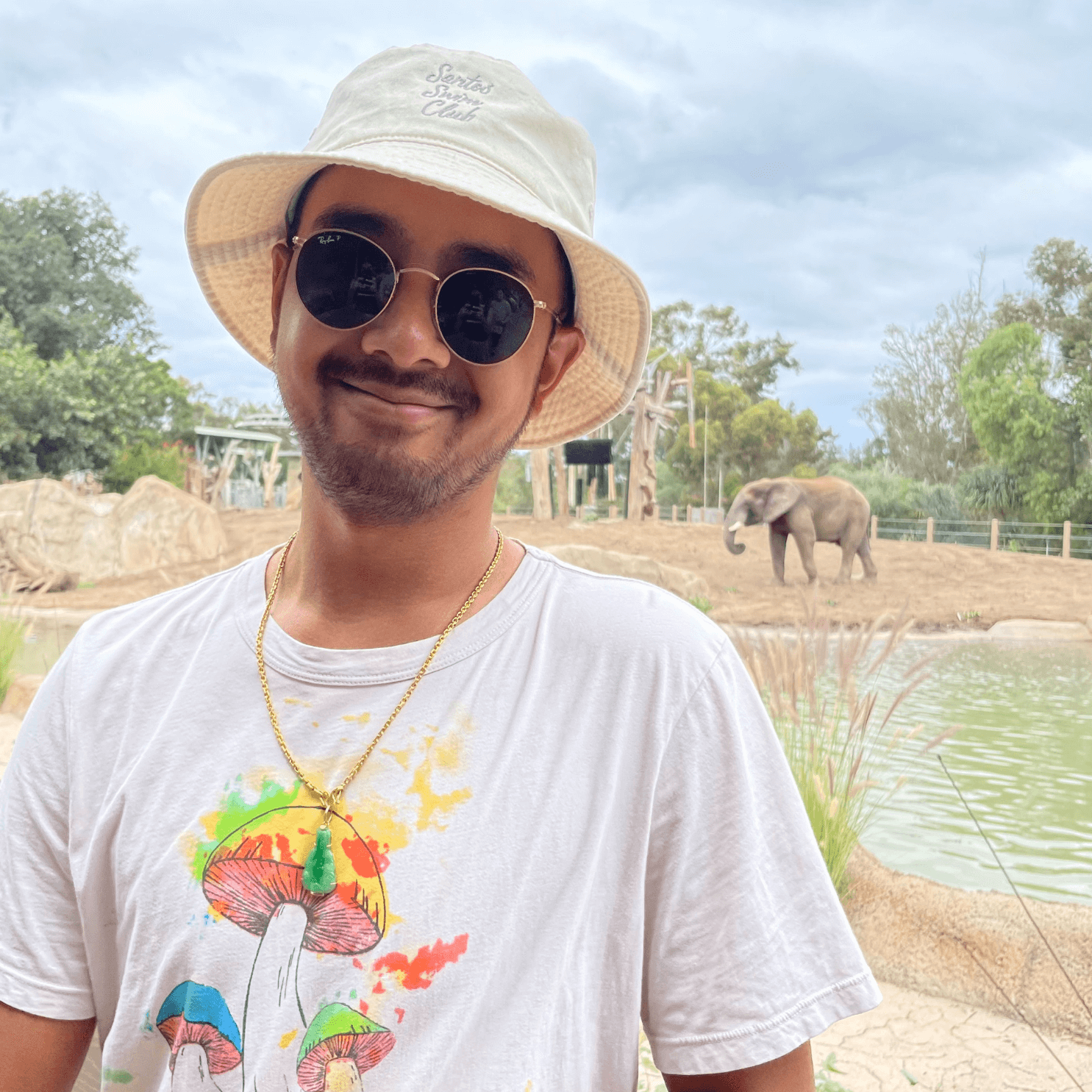 Man wearing unstructured ivory bucket hat with grey script embroidery Santos Swim Club